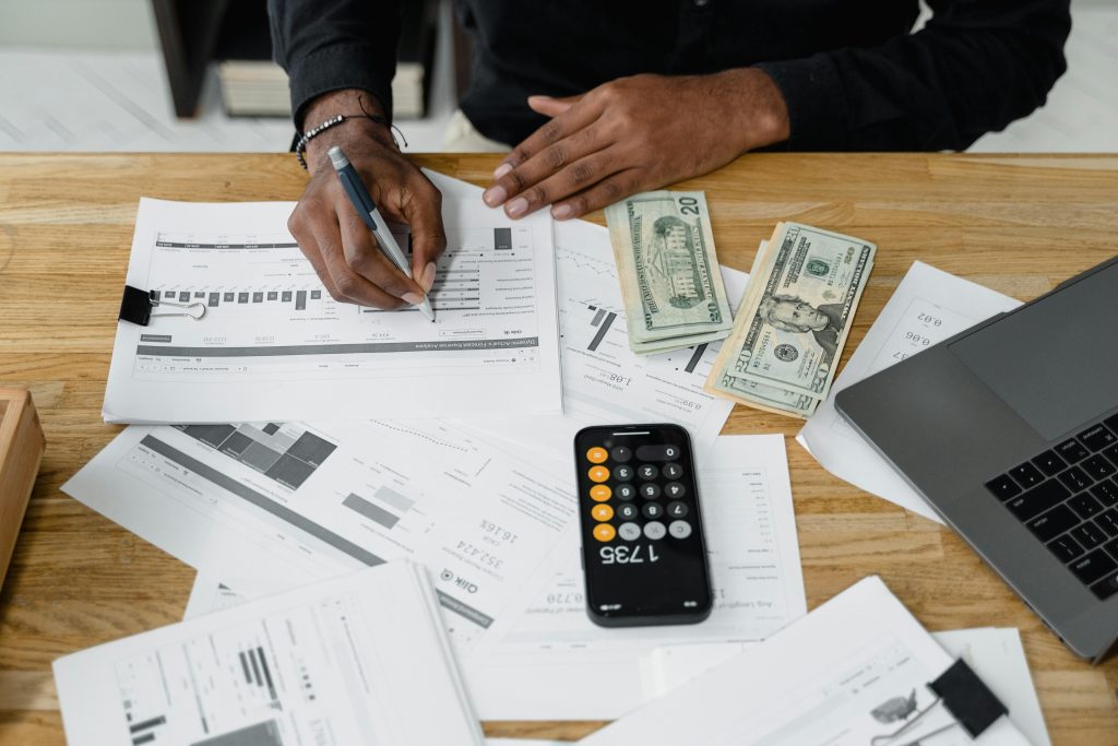pexels-photo-6694492-6694492 Man working on financial reports with calculator, money, and laptop on a desk.