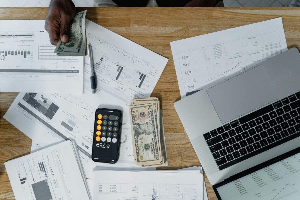 pexels-photo-6694950-6694950 Overhead view of a busy workspace with cash, financial documents, and a laptop.